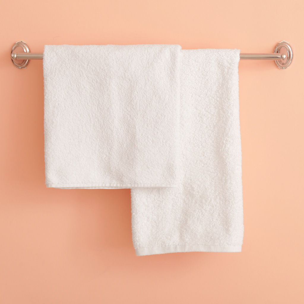 A pair of white bath towels hanging from a metal bar on a salmon pink wall